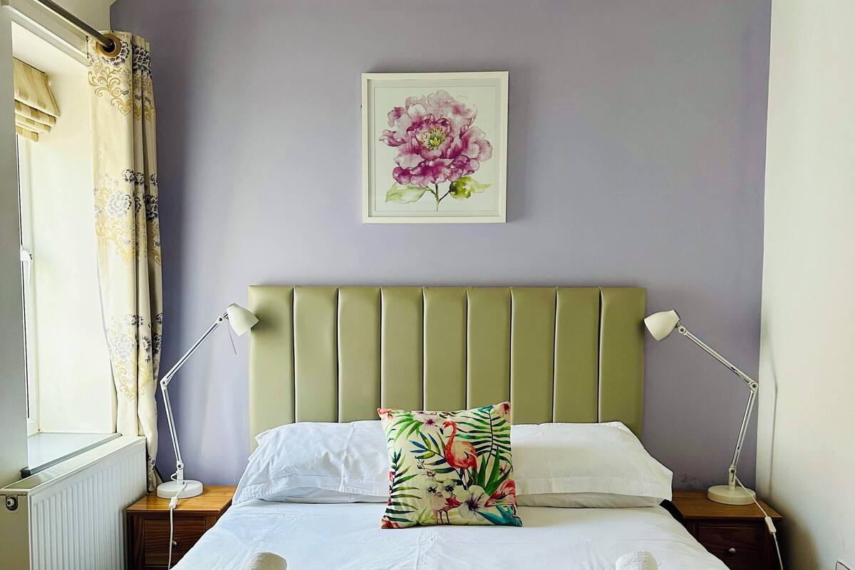 A neatly made bed with white linens, a floral pillow, and rolled towels.
