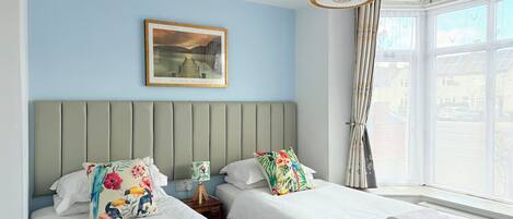 A hotel room with two beds, a large window with curtains, a ceiling light, and a framed picture on the wall.