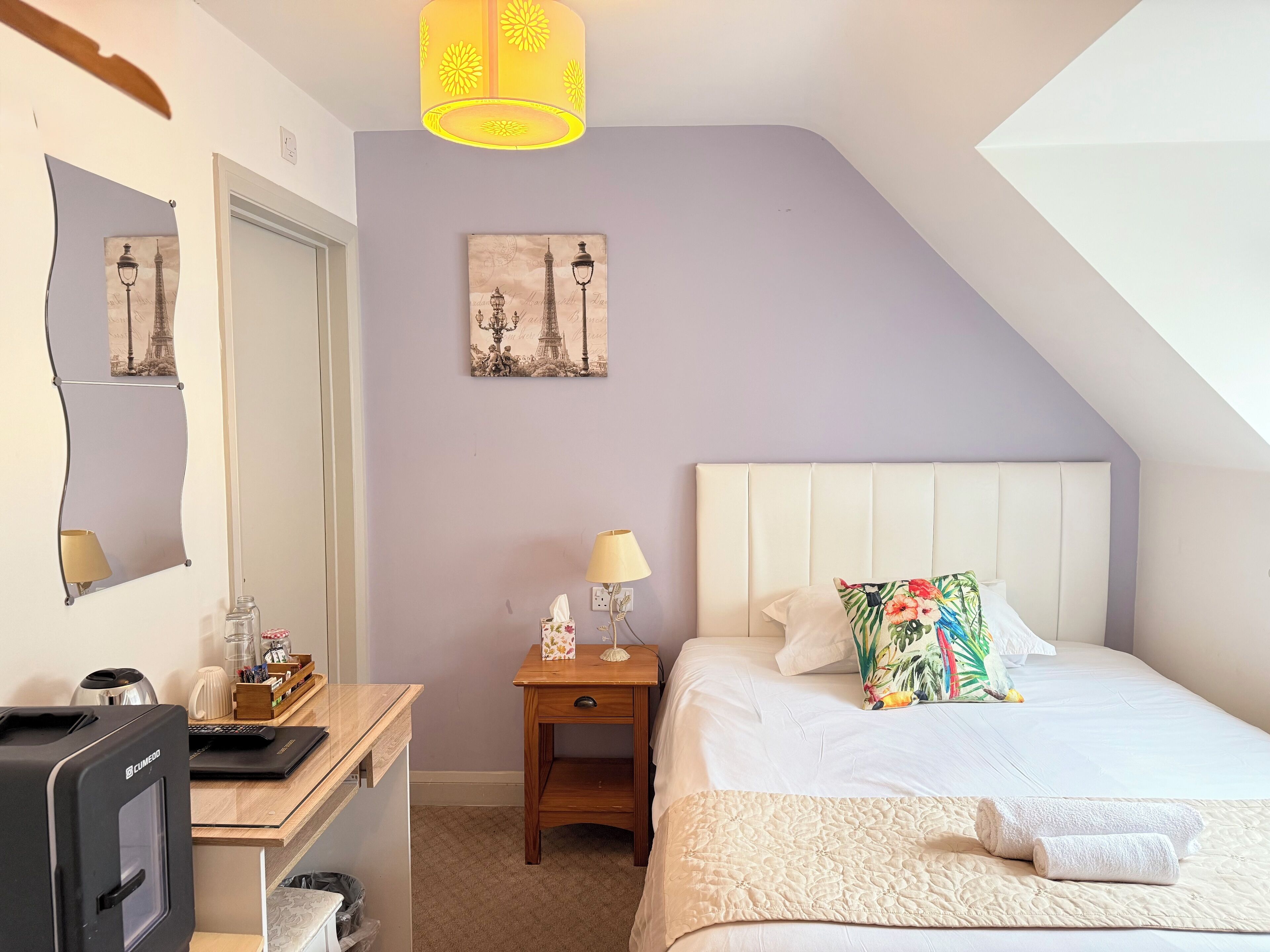A bedroom with a bed, bedside table, lamp, and a desk with a computer.
