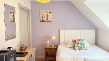 A bedroom with a bed, bedside table, lamp, and a desk with a computer.