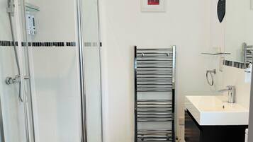A modern bathroom with a glass shower enclosure, a chrome towel rack, a white sink, and a mirror.