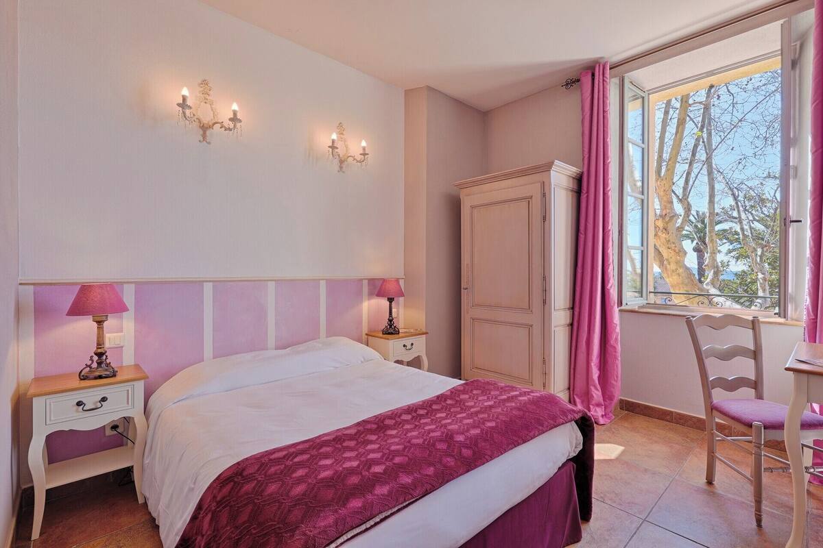 Un dormitorio con cama, dos mesitas de noche con lámparas, un armario, una silla y un ventanal con cortinas.
