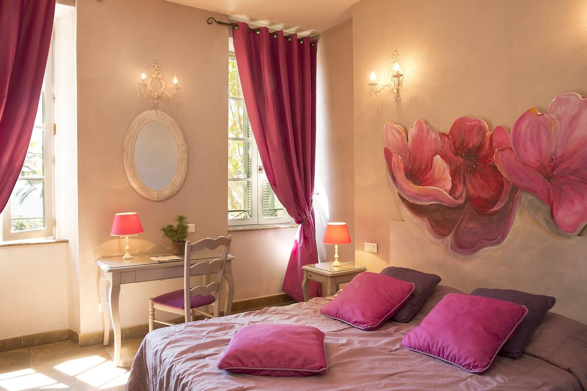 Un dormitorio con una cama, dos mesitas de noche, un escritorio, una silla y un gran mural floral en la pared.