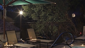 A poolside area with lounge chairs, an umbrella, and candles. - Hostellerie du Cigalou (Bormes-Les-Mimosas)