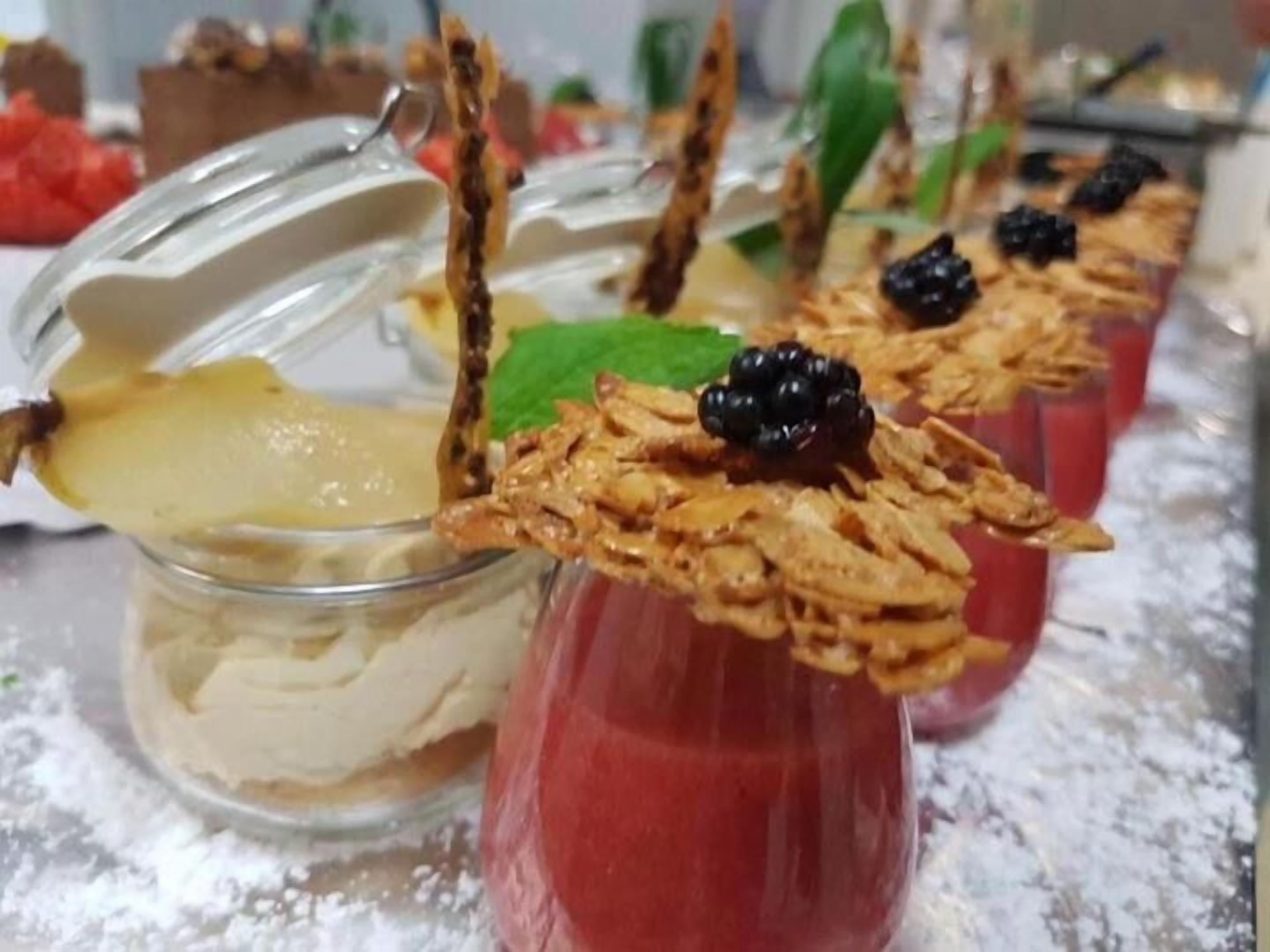 A dessert display with various treats, including a glass with a creamy dessert and a red drink topped with berries and granola.