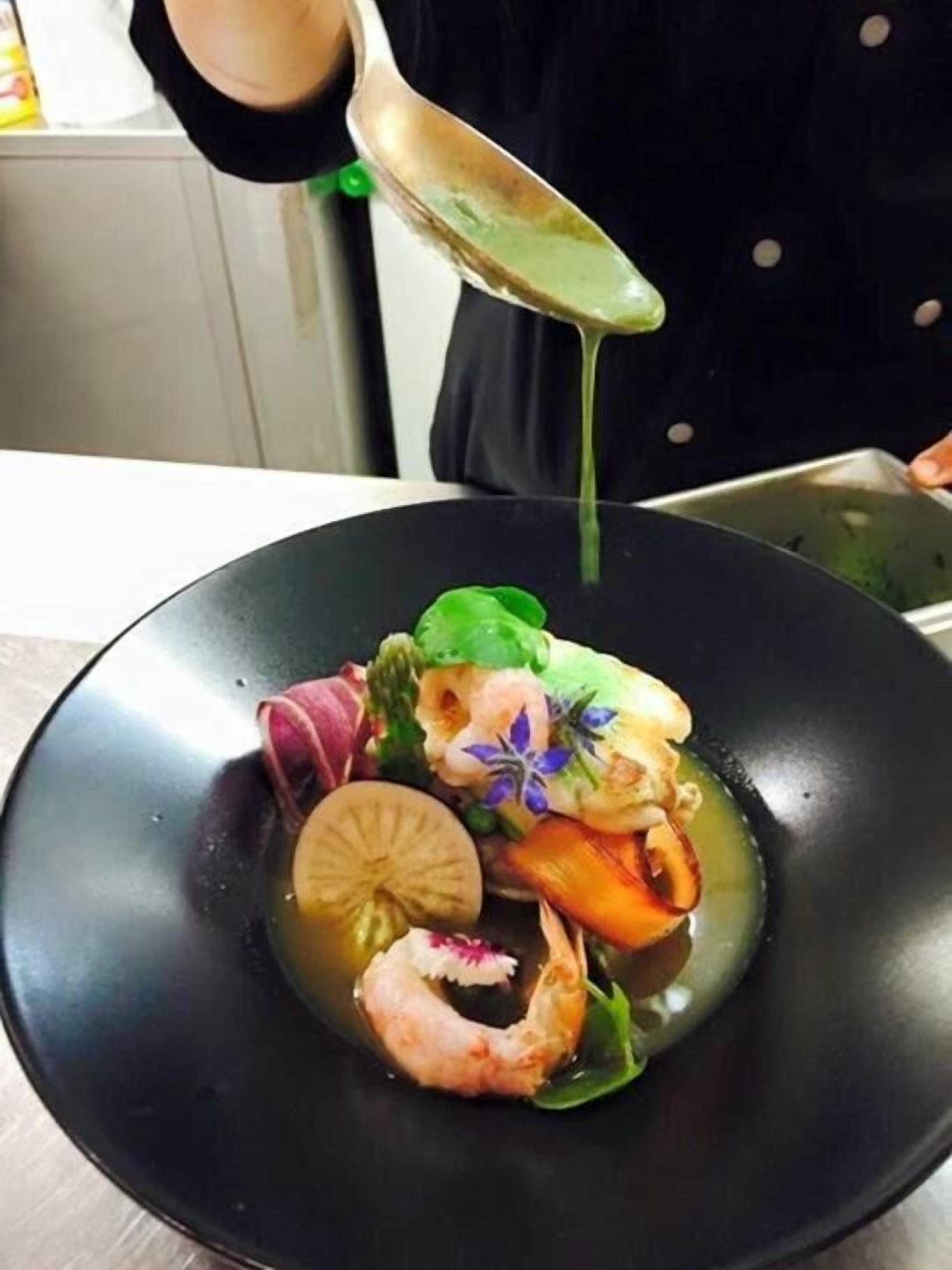 A person pouring a green sauce over a dish with seafood and vegetables.