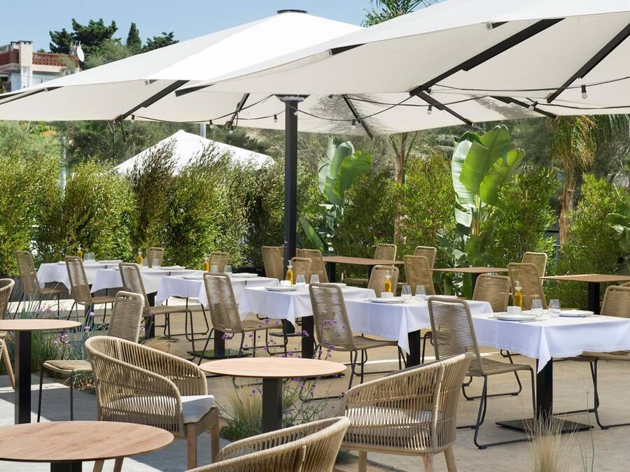 Un espace de restauration en plein air, avec des tables et des chaises, protégé par de grands parasols et entouré de verdure.