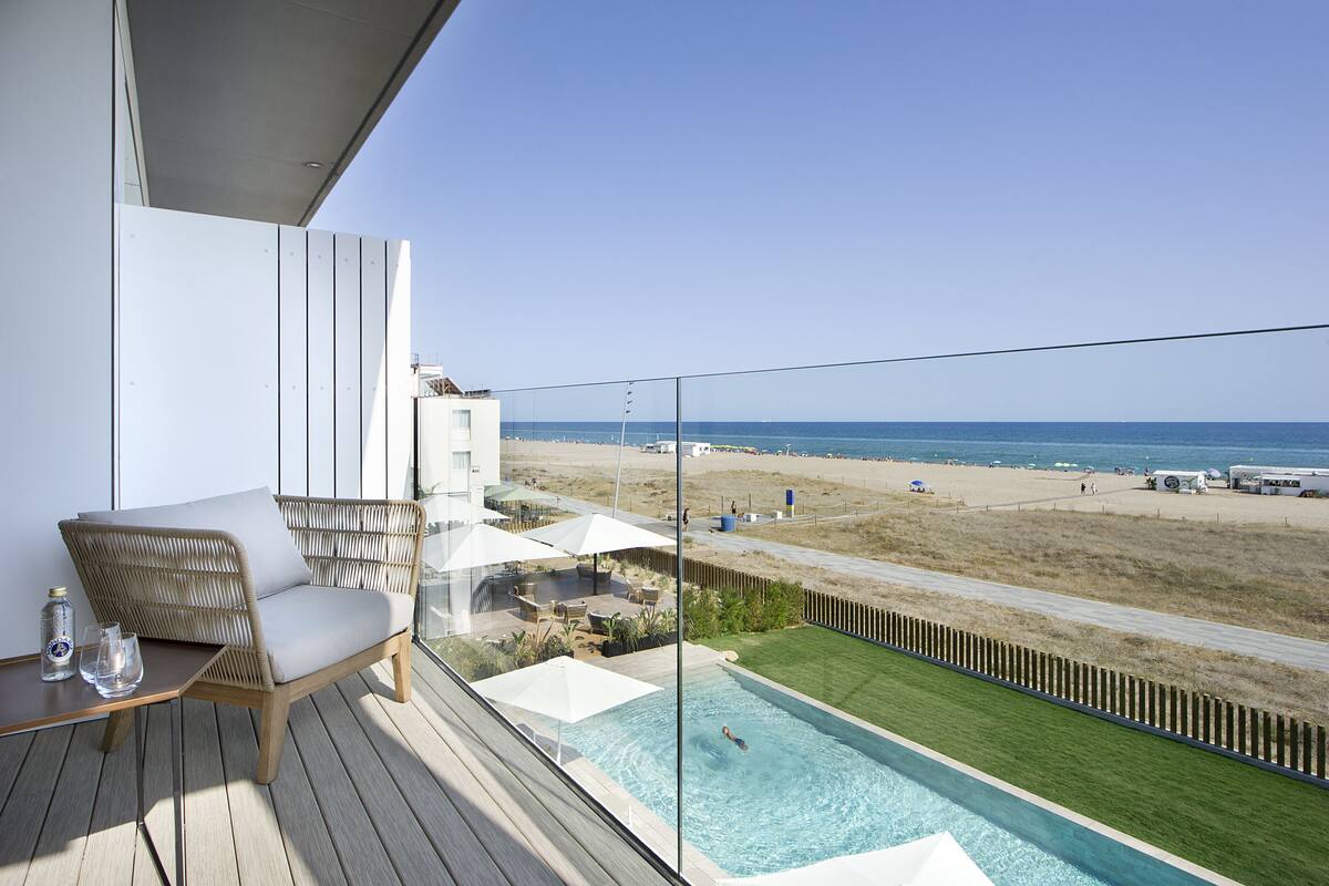 Un balcon avec un fauteuil en osier, une petite piscine et une vue sur la plage.