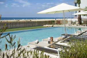 Una piscina al aire libre, sombrillas, sillones reclinables de piscina