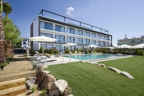 Un hotel moderno con piscina, tumbonas y un césped bien cuidado.
