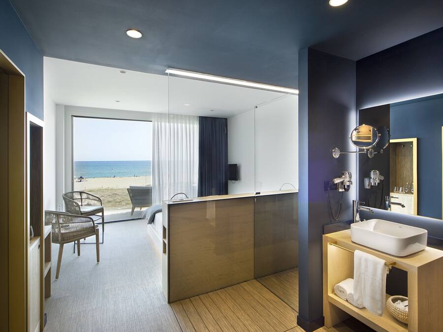 A modern bathroom with a large mirror, a sink, and a shower area. There is a balcony with a view of the beach.