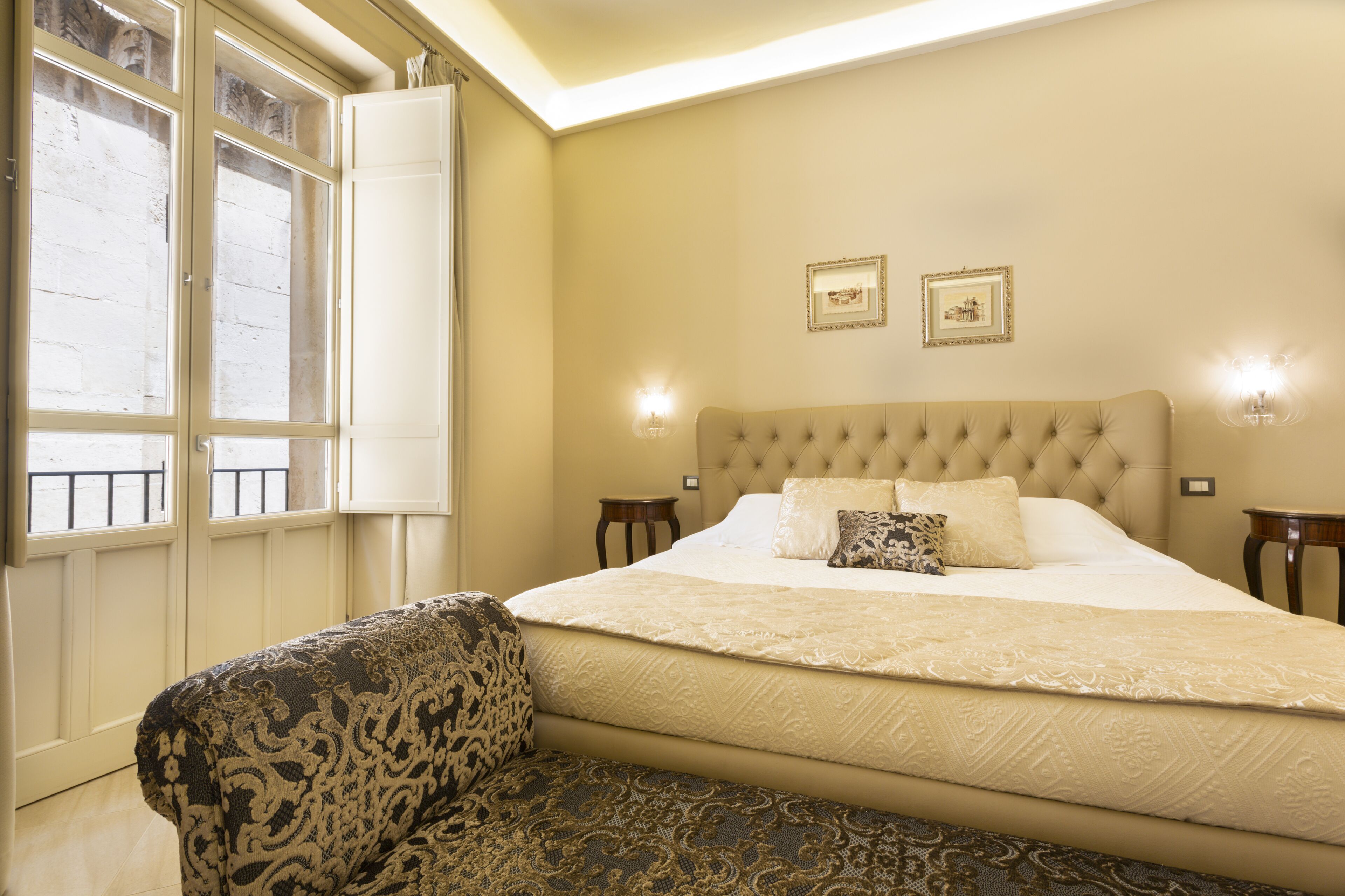 Un dormitorio con una cama grande, un sillón estampado y dos lámparas de pared.