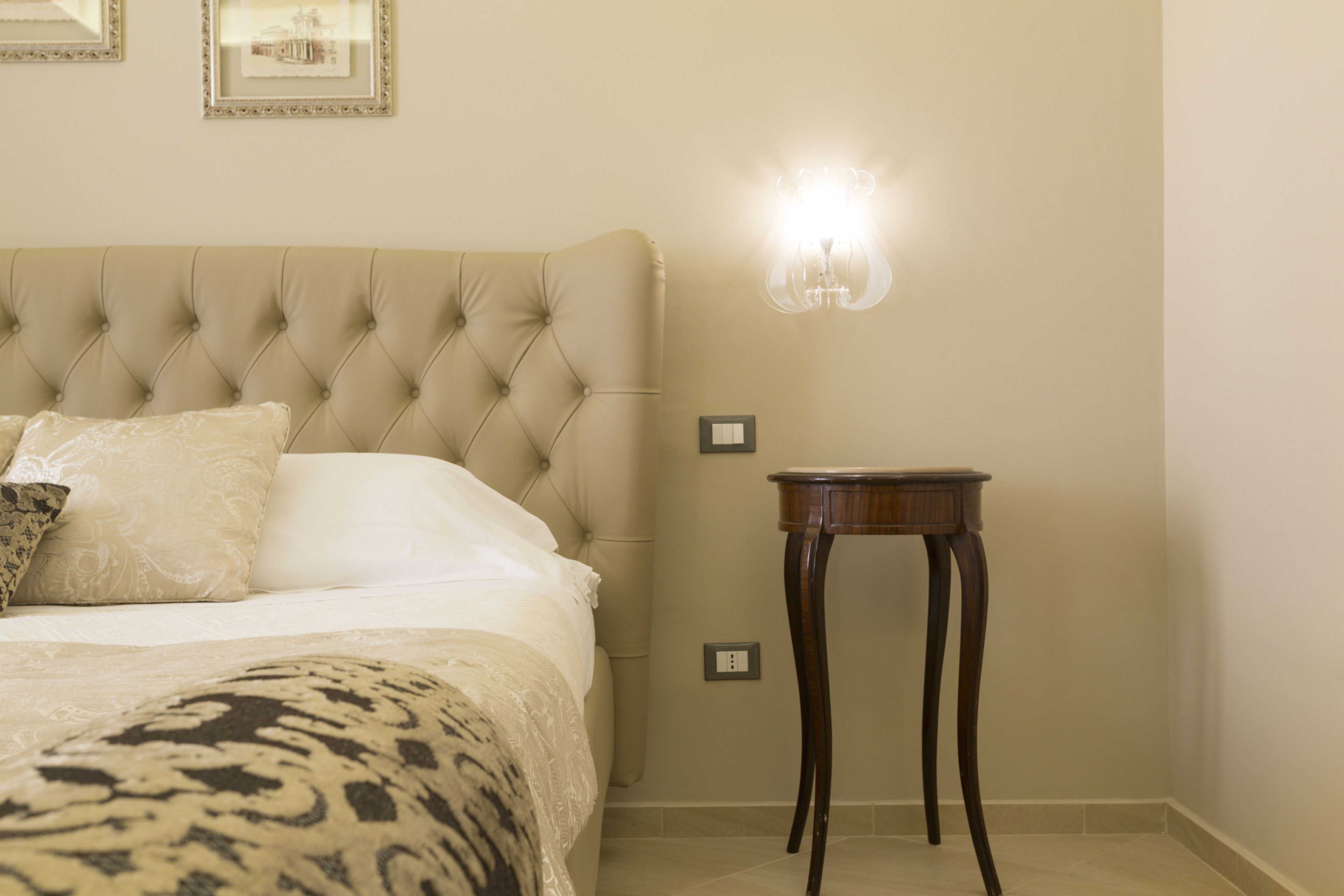 A neatly made bed with a tufted headboard, a bedside table, and a wall-mounted light fixture.