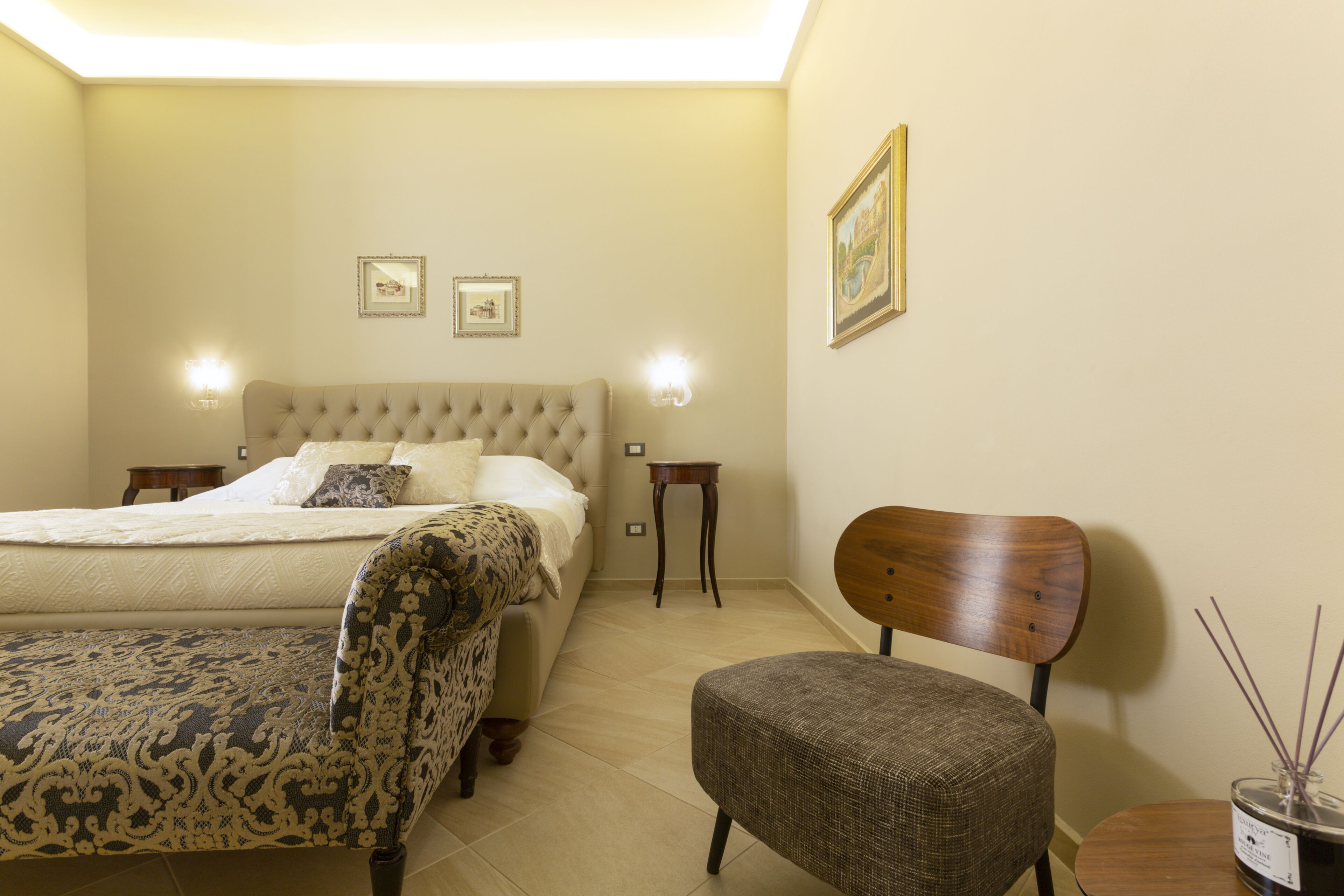 A bedroom with a bed, a chair, a small table, and a nightstand.