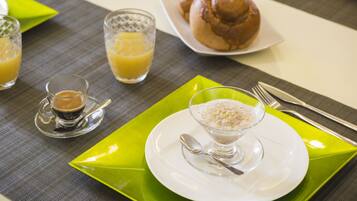 A breakfast setting with a plate of rolls, a glass of orange juice, and a bowl of cereal.