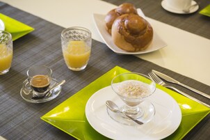 A breakfast setting with a plate of rolls, a glass of orange juice, and a bowl of cereal.