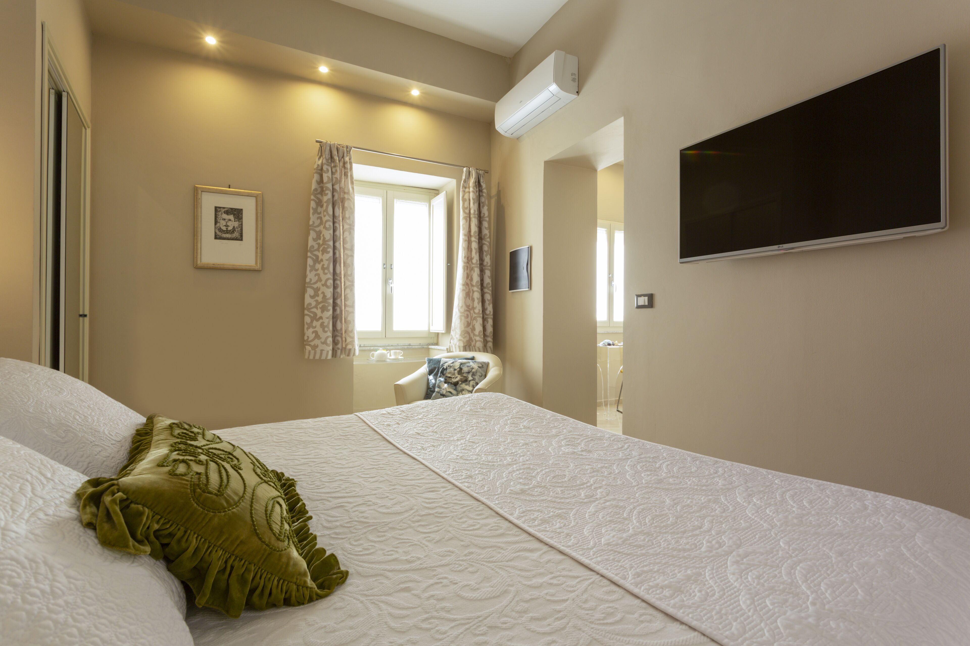A hotel room with a large bed, a flat-screen TV mounted on the wall, and a window with curtains.