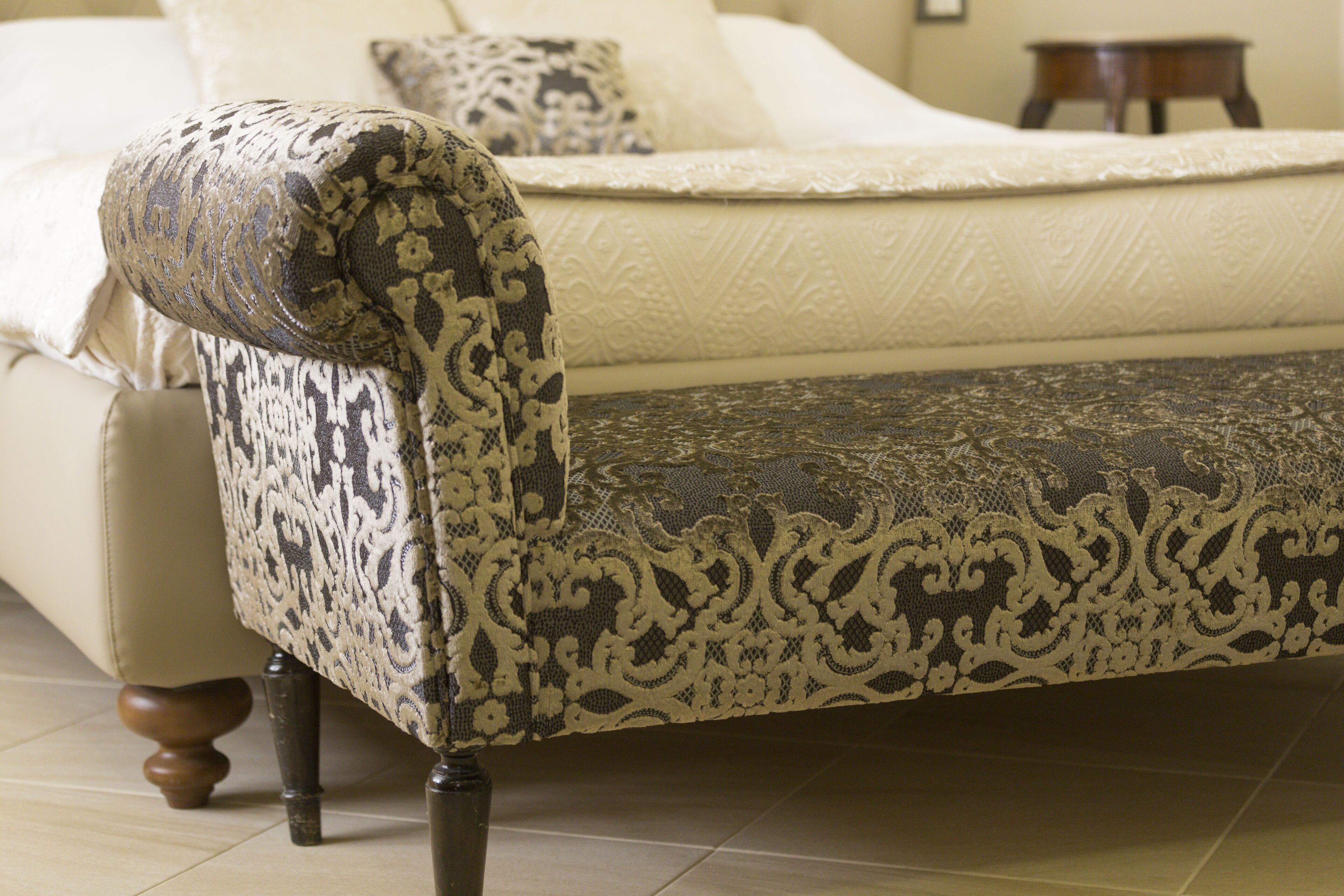 Un dormitorio con cama, un sillón estampado y una mesita de madera.