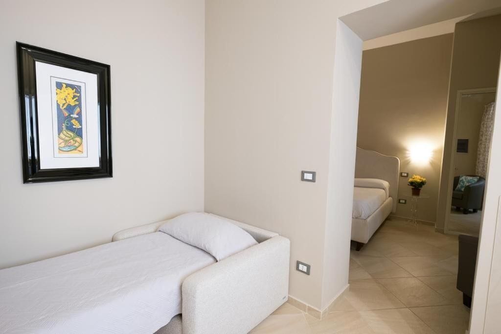 A small, compact room with a single bed, a framed artwork on the wall, and a small table with a plant.