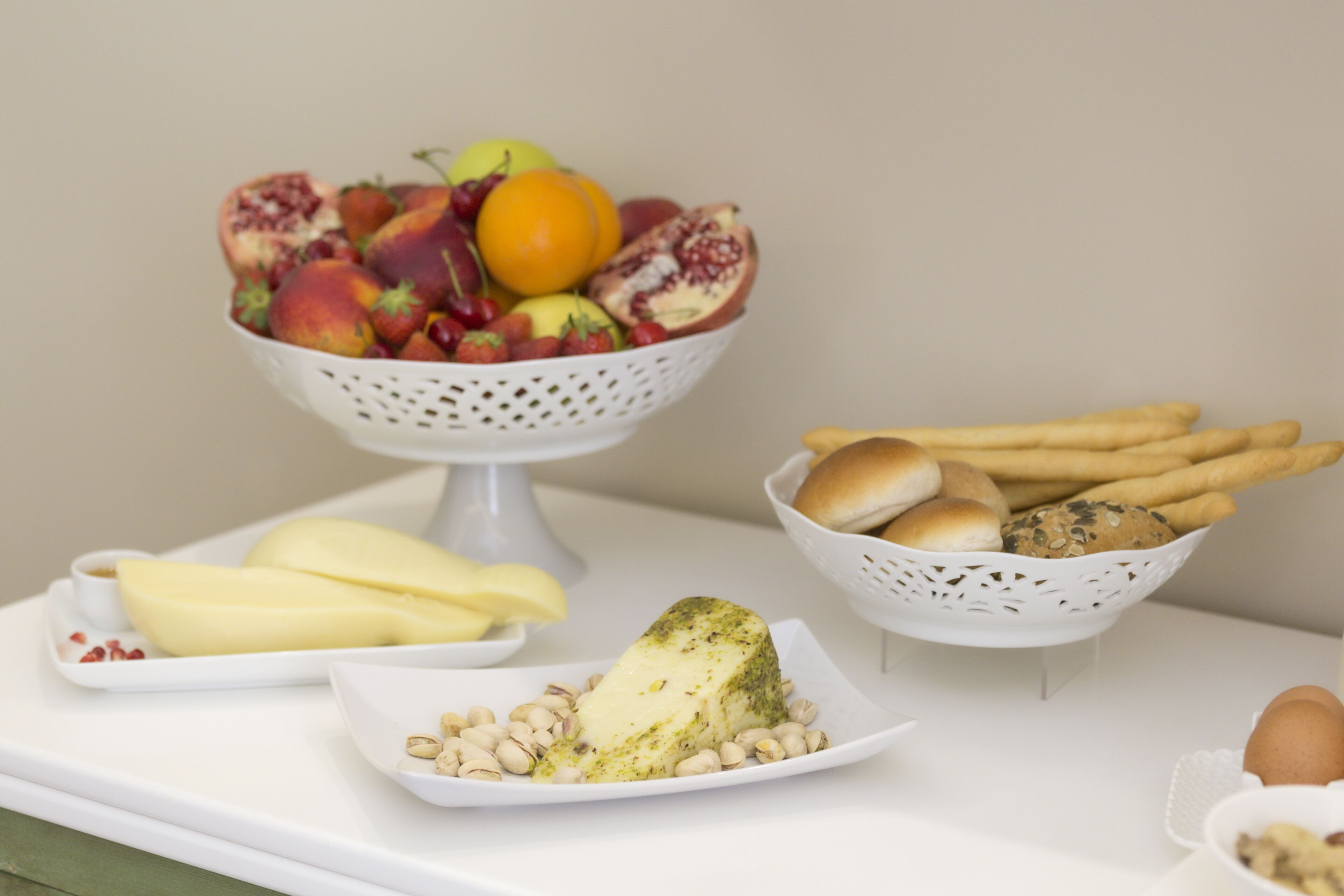 Une table avec un panier de fruits, une assiette de fromage et un panier de pain.