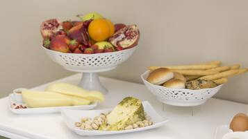 Une table avec un panier de fruits, une assiette de fromage et un panier de pain.