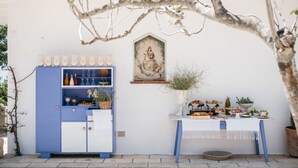 A blue cabinet with various kitchenware, a white table with food and drinks, and a religious painting on the wall. - Villa de Donatis Charming Guest House (Casarano)