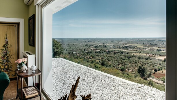 A balcony with a view of a rural landscape, a wooden door, and a small table with a vase of flowers. - Villa de Donatis Charming Guest House (Casarano)