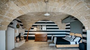 A room with a stone vaulted ceiling, striped walls, a sofa, and a wooden dresser. - Villa de Donatis Charming Guest House (Casarano)