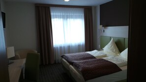 A hotel room with a bed, a desk, a chair, and a window with curtains.