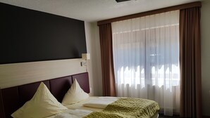 Une chambre d’hôtel avec un lit, une tête de lit, une fenêtre avec des rideaux et un luminaire fixé au mur.