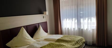 Een hotelkamer met een bed, hoofdeinde, raam met gordijnen en een wandlamp.