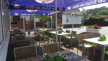 An outdoor seating area with tables and chairs, umbrellas, and a brick wall in the background.