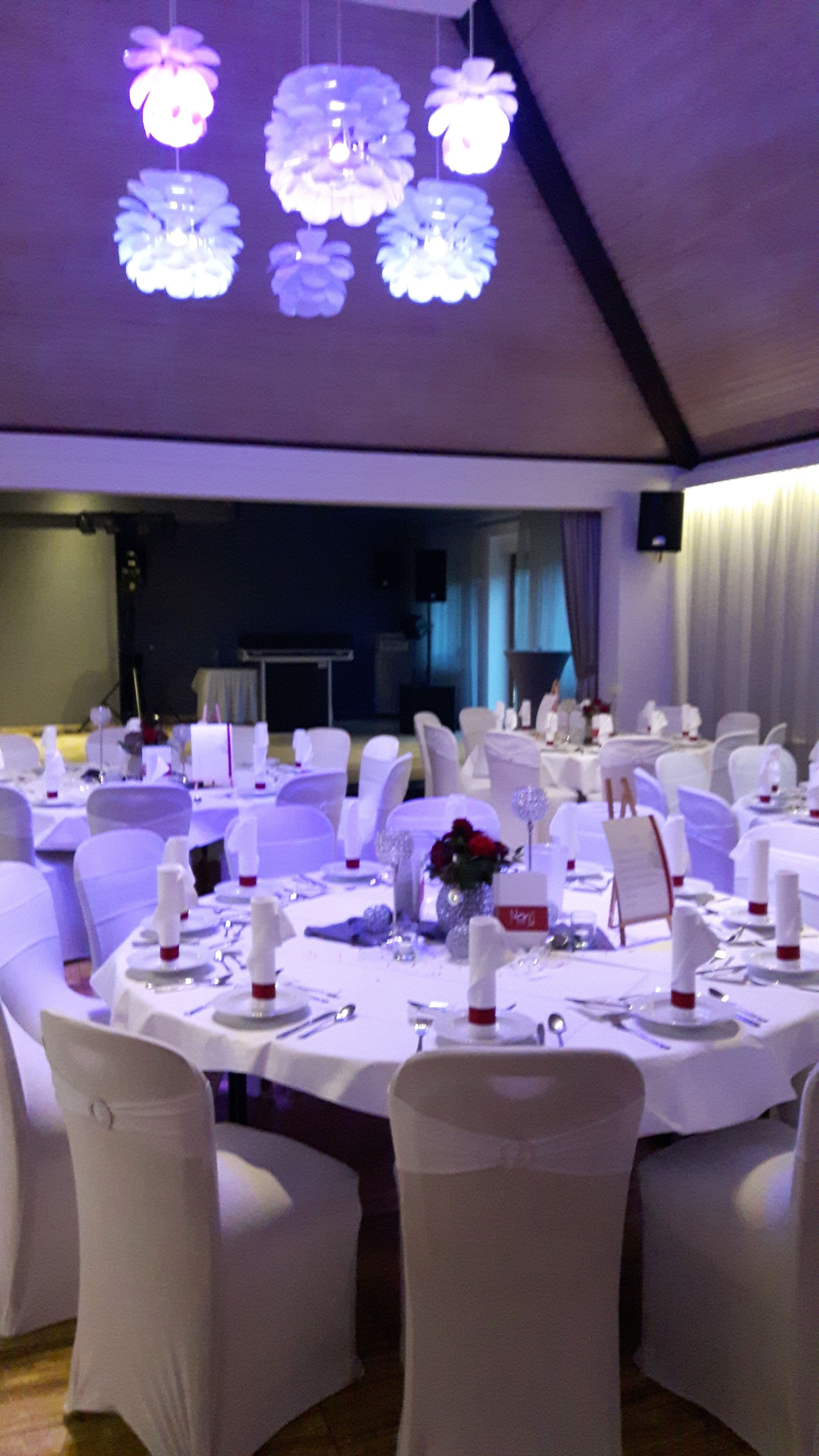 A banquet hall with round tables set for dining, white chairs, and overhead lighting.