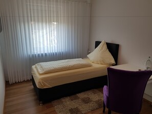 A bedroom with a bed, a chair, a desk, and a window with curtains.