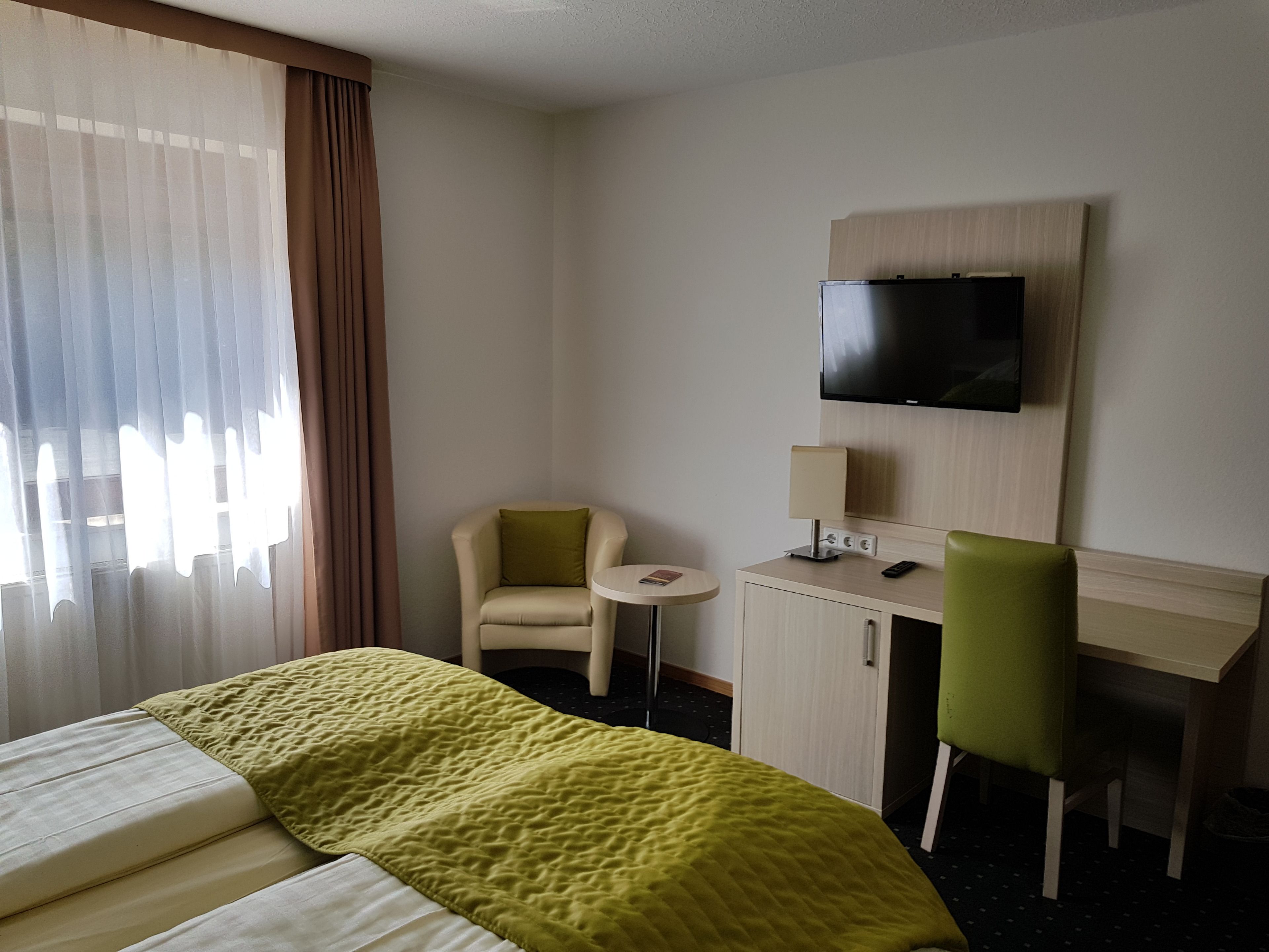 Una habitació d'hotel amb llit, escriptori, cadira, televisió i taula petita.