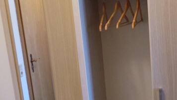 Un vestidor con perchas de madera en una barra, un espejo y una puerta con manija.