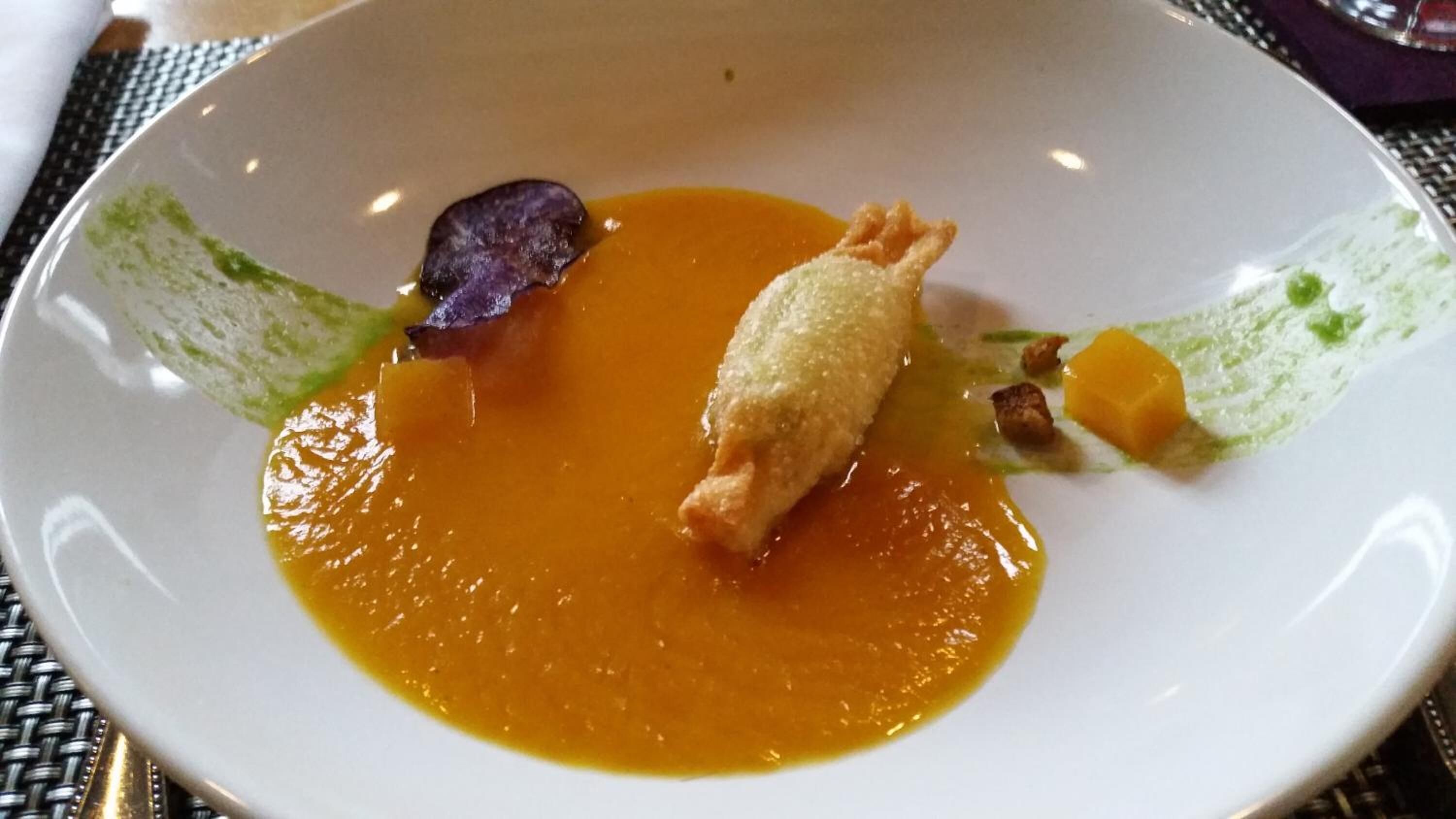 A white plate with a soup, a piece of bread, and some vegetables.