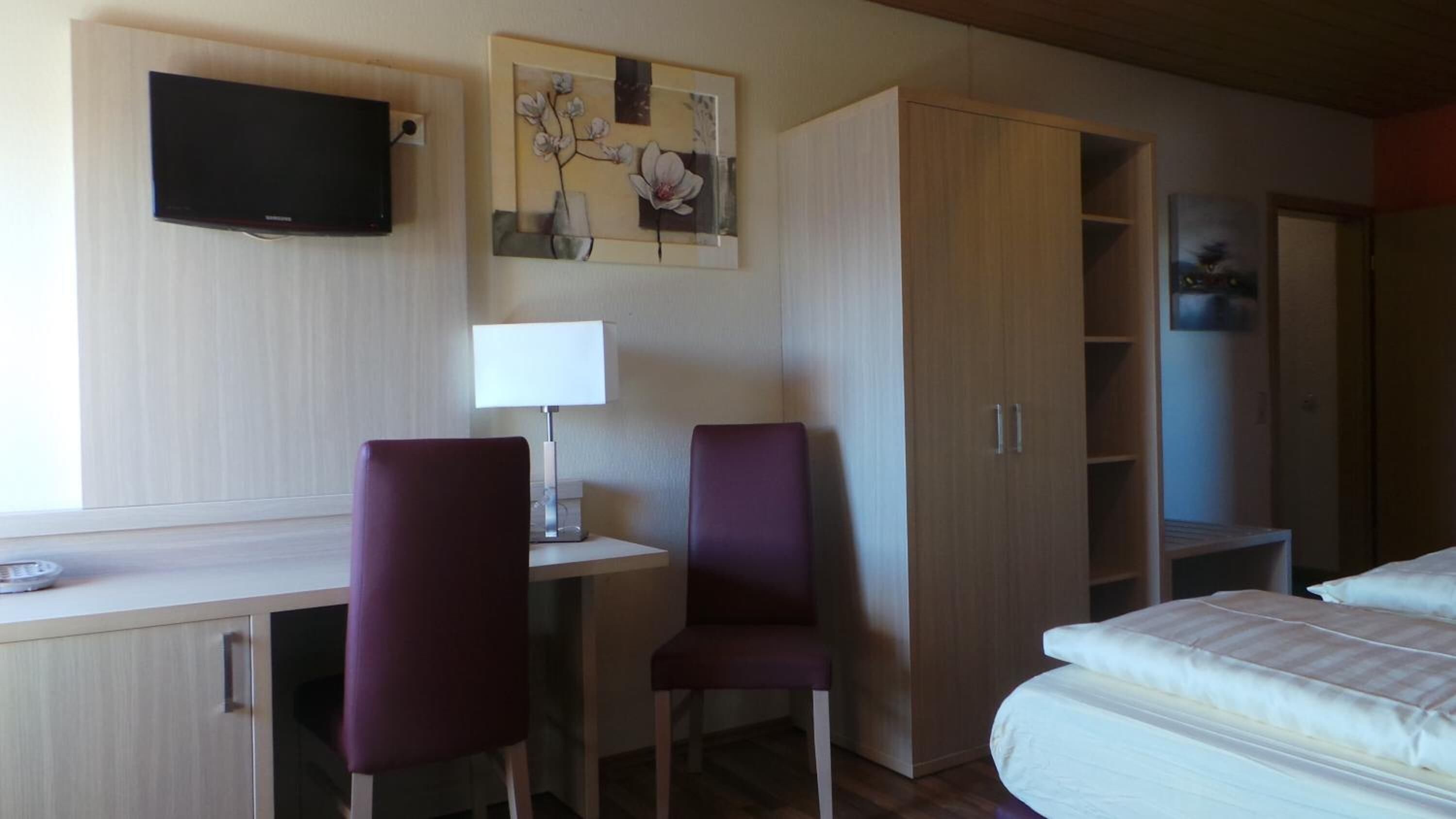 Ett hotellrum med en säng, ett skrivbord med två stolar, en tv och en garderob.