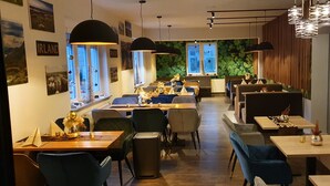 Un restaurant doté de nombreuses tables et chaises, d’un mur végétal agrémenté de fenêtres et de luminaires suspendus.