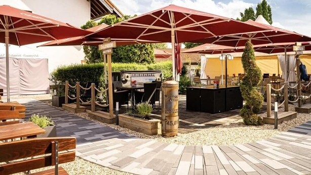 Un espace extérieur aménagé en terrasse, avec des bancs en bois, des parasols rouges et un coin barbecue.