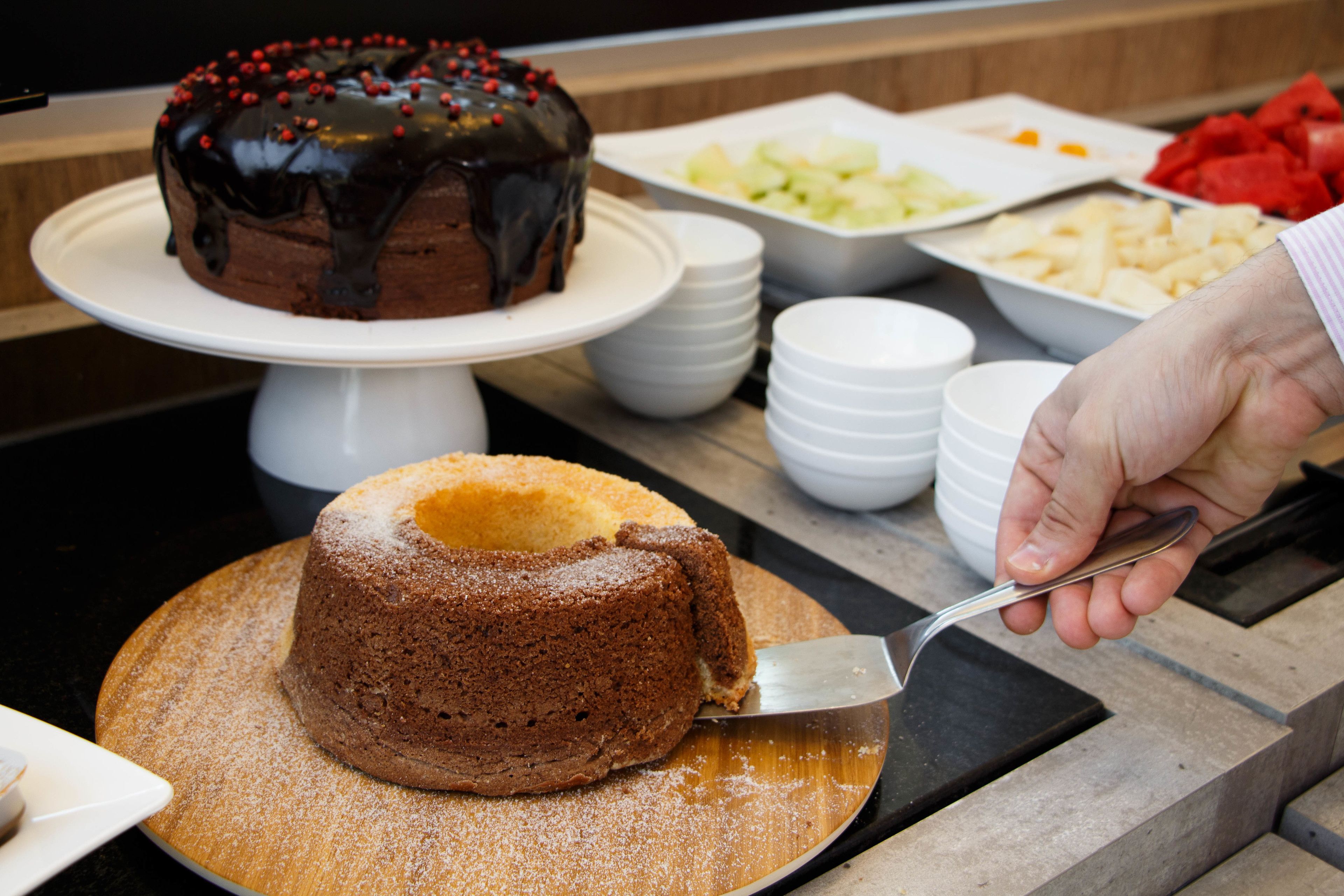 A cake on a white stand with a person using a spatula to cut it.