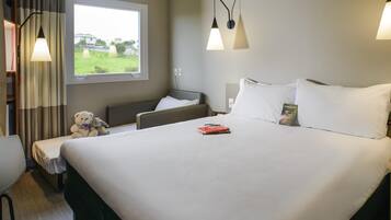 A hotel room with a large bed, bedside tables, a chair, a window with curtains, and wall-mounted lamps.