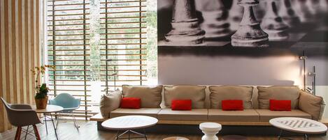 A modern living room with a beige sofa, red cushions, a round coffee table, and a chessboard mural on the wall.