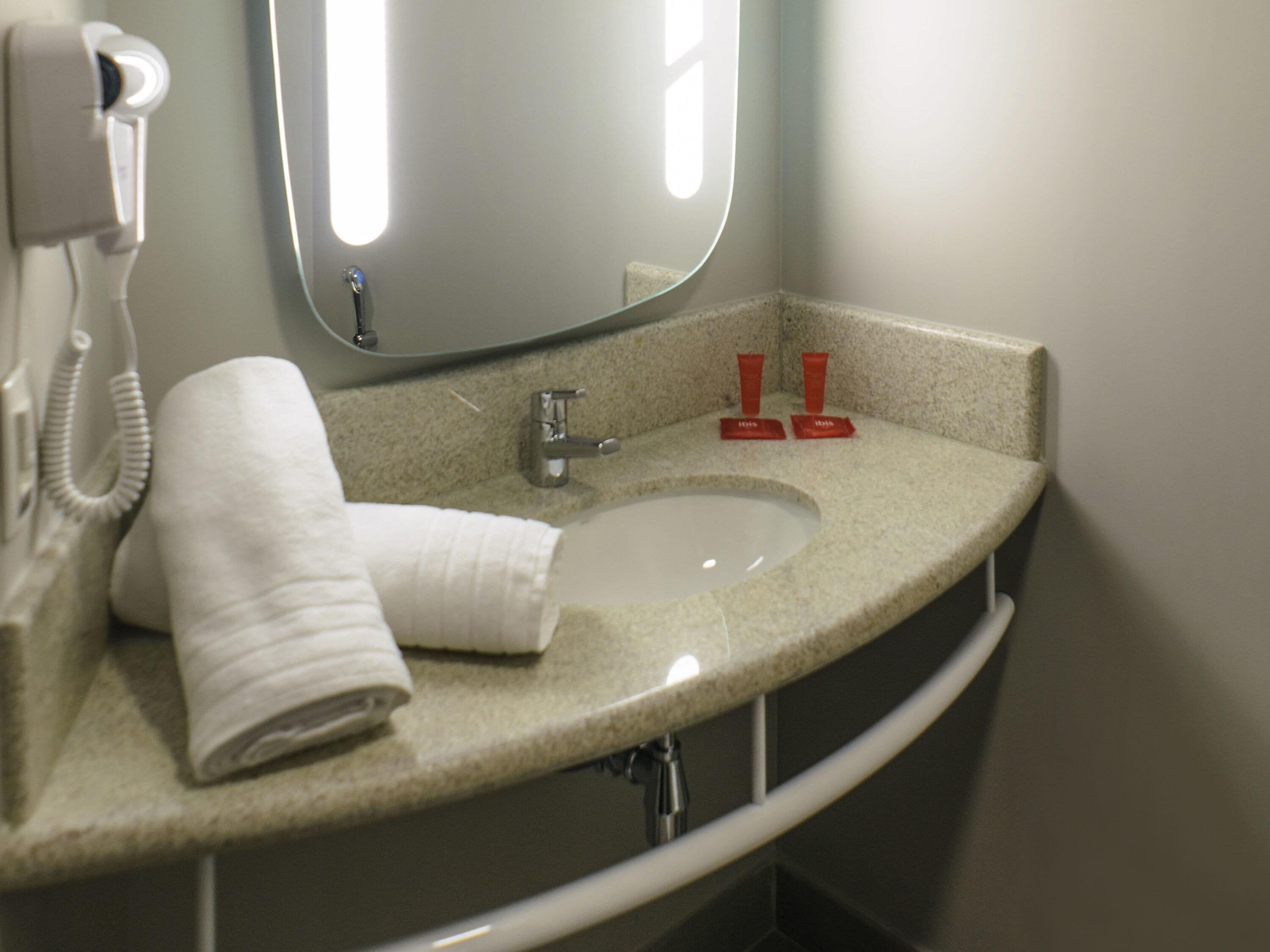 Un baño con lavamanos, espejo, toalla y secador de pelo.