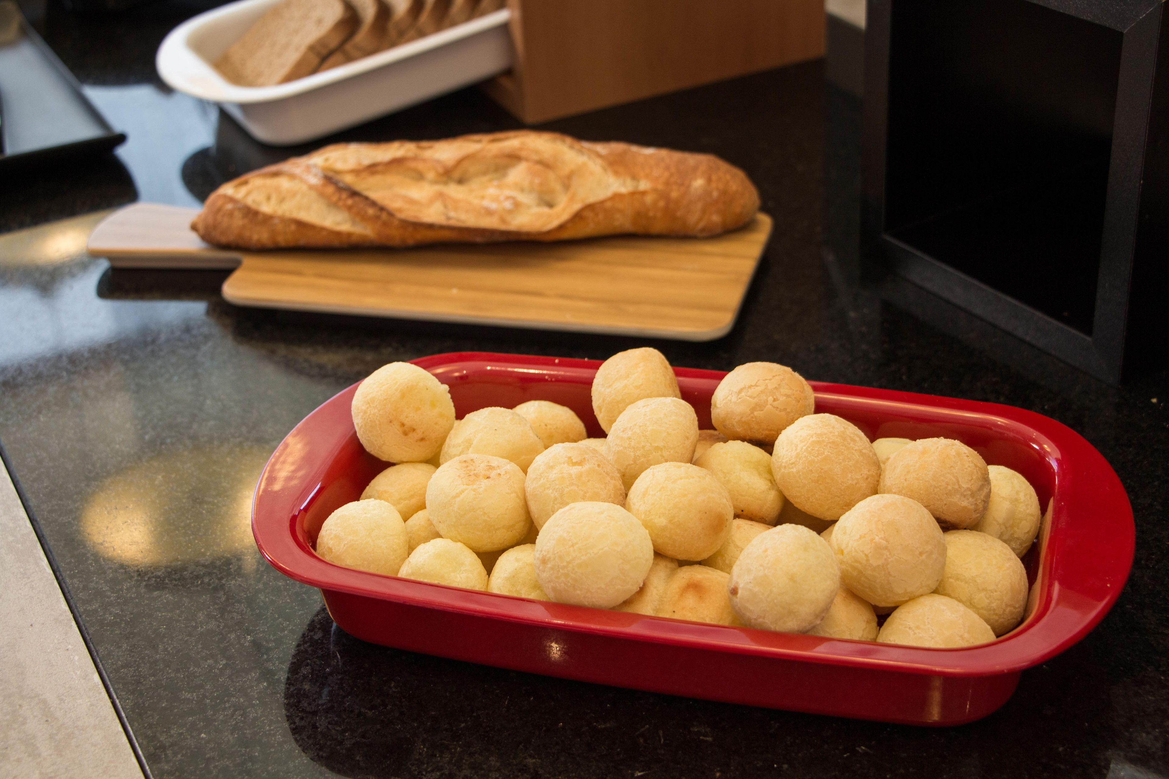 A kitchen counter with a red baking dish filled with dough balls, a loaf of bread on a cutting board, and a microwave in the background.