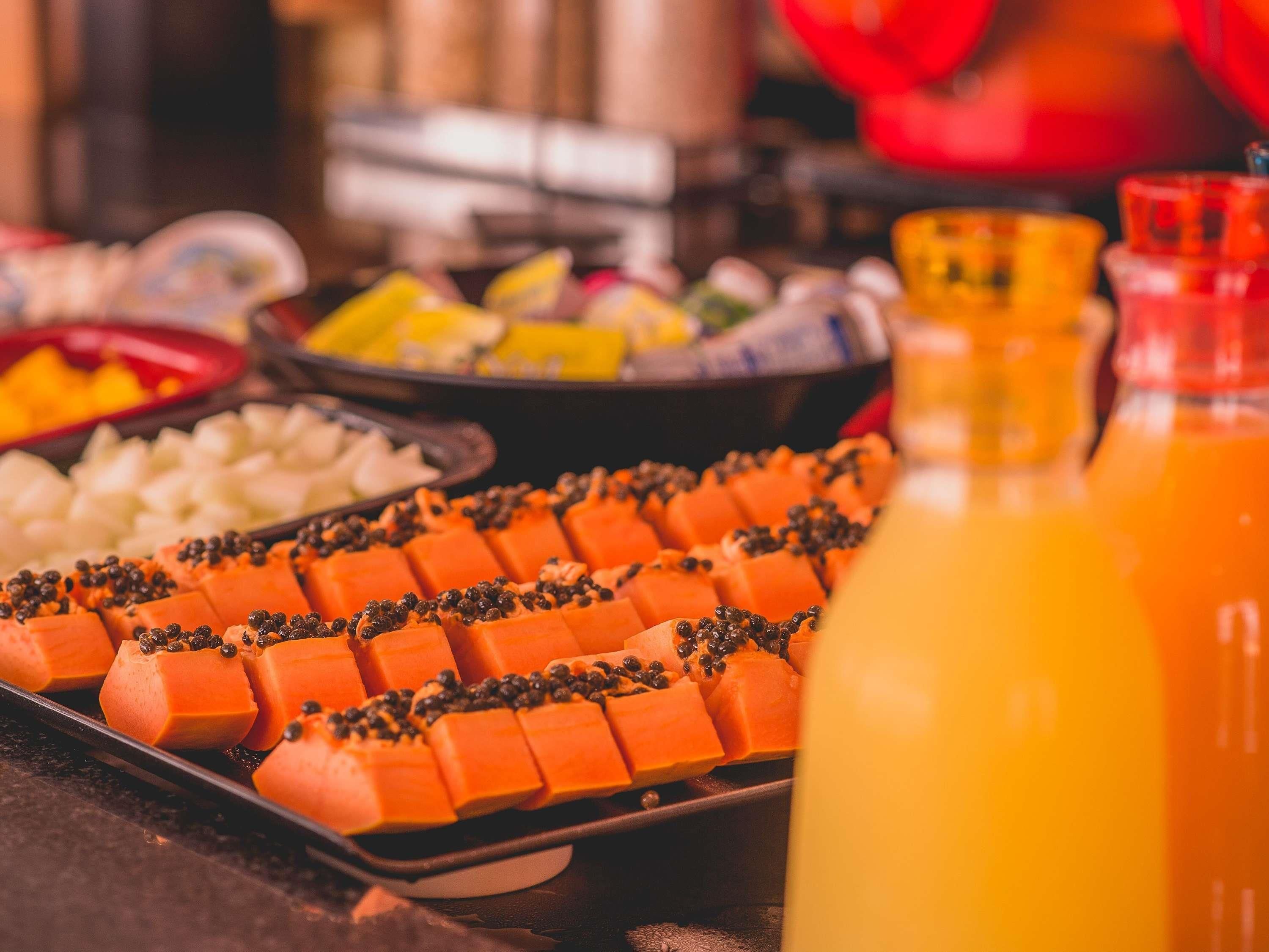 Un bufé con diversos alimentos, incluyendo cubos de comida anaranjada, posiblemente queso, y una botella de jugo de naranja.