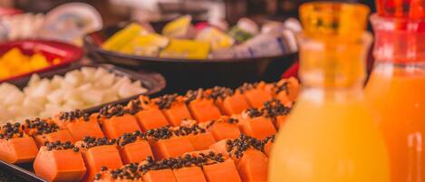 Un bufé con diversos alimentos, incluyendo cubos de comida anaranjada, posiblemente queso, y una botella de jugo de naranja.
