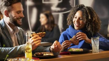 Una pareja cenando en un restaurante con ambiente informal, que cuenta con una mesa de madera, una bebida y un sándwich.