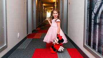 Um corredor de hotel com carpete vermelho, portas em ambos os lados e um brinquedo de pelúcia do Mickey na parede.