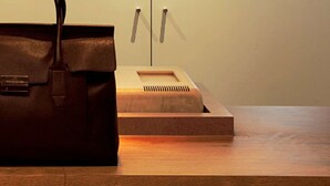A brown leather bag on a wooden table with newspapers. - Ibis Carlos Barbosa (Carlos Barbosa)